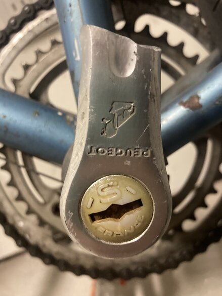 Broken bicycle pedal with Peugeot logo upside down. Bike frame in the background